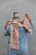 Woman wearing multicolored striped scarf, 52 Weeks of Scrap Yarn knitting pattern, blue denim shirt, gray background.