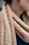 Multicolored knitted scarf in light beige with pastel hues, wrapped around neck, featuring intricate cable patterns and subtle color accents.