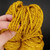 Close-up of Happiness golden ochre handspun merino yarn held between fingers to show bulky weight and individual plied strands.