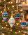Four vintage-inspired handmade felted wool Christmas ornaments hanging on an evergreen tree with warm holiday lights.