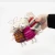 Hand holding three felted wool sheep ornaments in rainbow striped, pink striped, and red and gray striped knitted sweaters.