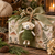 Felted wool sheep ornament in a moss green sweater tied to a woodland floral wrapped gift with sage ribbon and greenery.