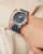 Baume & Mercier Riviera Tideograph 10761 on wrist — 43 mm steel case with blue sun-ray dial, tide-indicator display, and integrated blue rubber strap showcasing sport-luxury style.