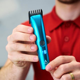 Seabreeze Blue Andis EMERGE® Trim Cordless Trimmer held in hand with an adjustable attachment comb installed.