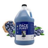 Gallon jug of Bark2Basics Face Furst Facial Scrub, displayed with fresh blueberries rolling out of a wooden basket