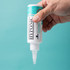 Close-up of ear cleaner bottle held upside down with drop dispensing from nozzle against a teal background