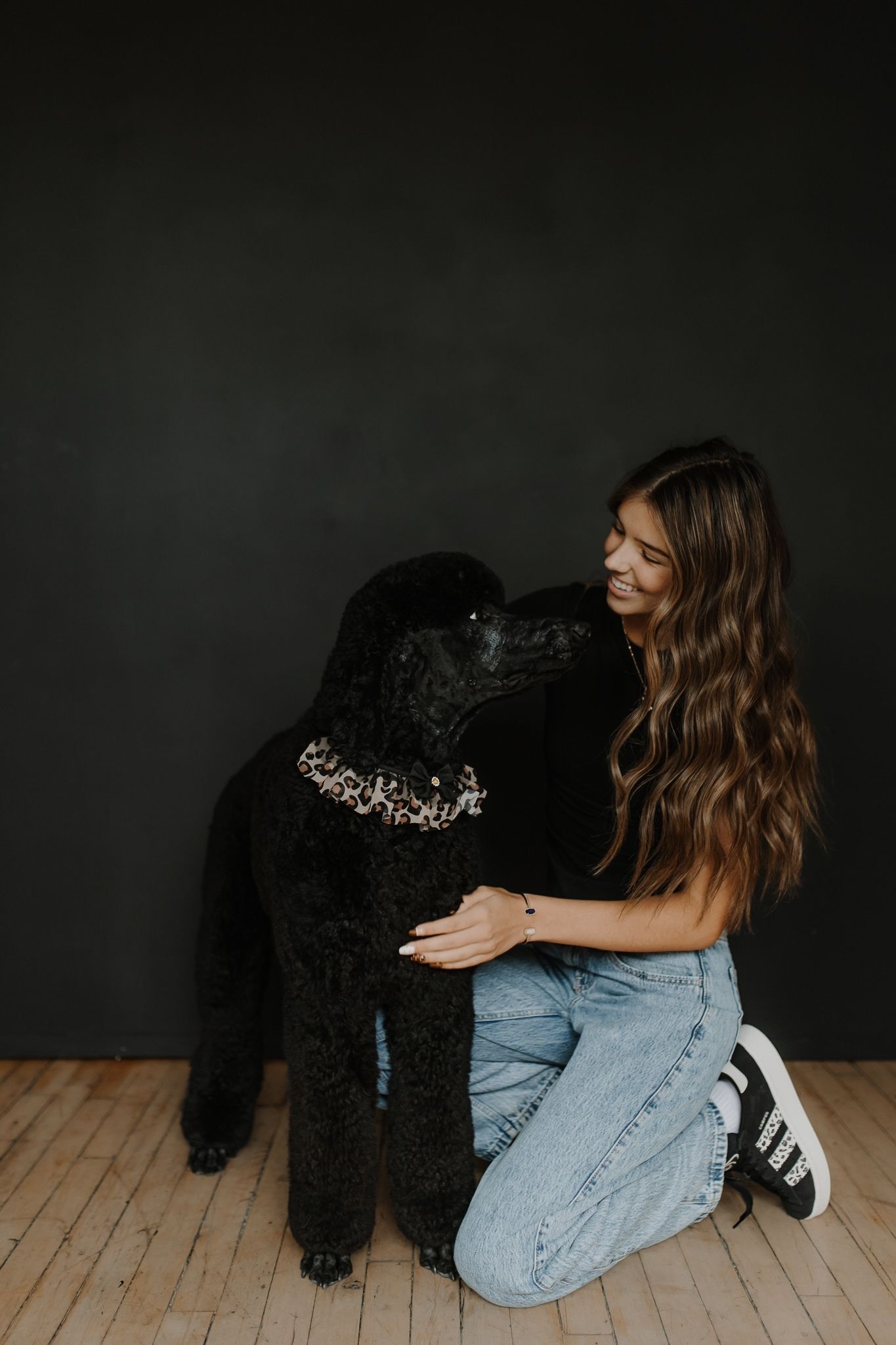 Johanna Ogreen and a black Standard Poodle together on a wooden floor against a black backdrop