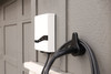White Emporia Pro EV charger mounted on the exterior wall of a house with its charging cable neatly hung on a wall-mounted holder on the side.