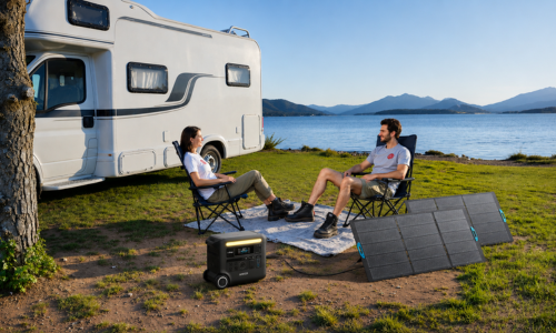 Two people sitting outside RV with Anker SOLIX portable power station and lake and mountains in the distance.