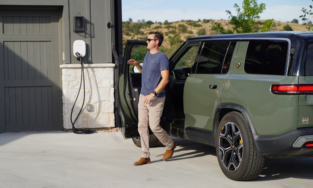Man exiting electric vehicle in blue and white with an Emporia charger mounted by garage.