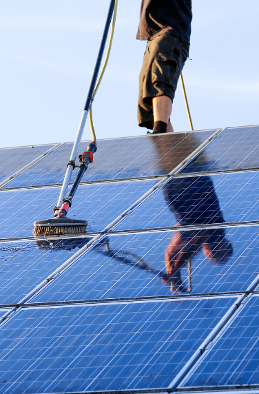Person cleaning solar panels on roof with brush.