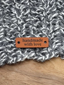 Custom Faux Leather Labels with Your Own Design | 0.5" x 1.5" Sew-On Tags (set of 25), brown faux leather sew-on tag reading “handmade with love” displayed on a gray-and-white knitted fabric