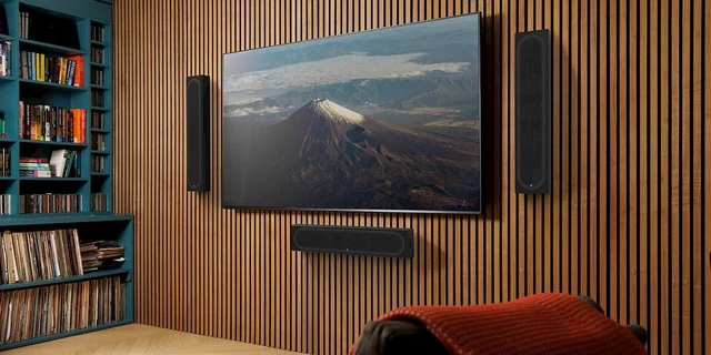 Large wall-mounted TV with on-wall speakers on a timber acoustic feature wall