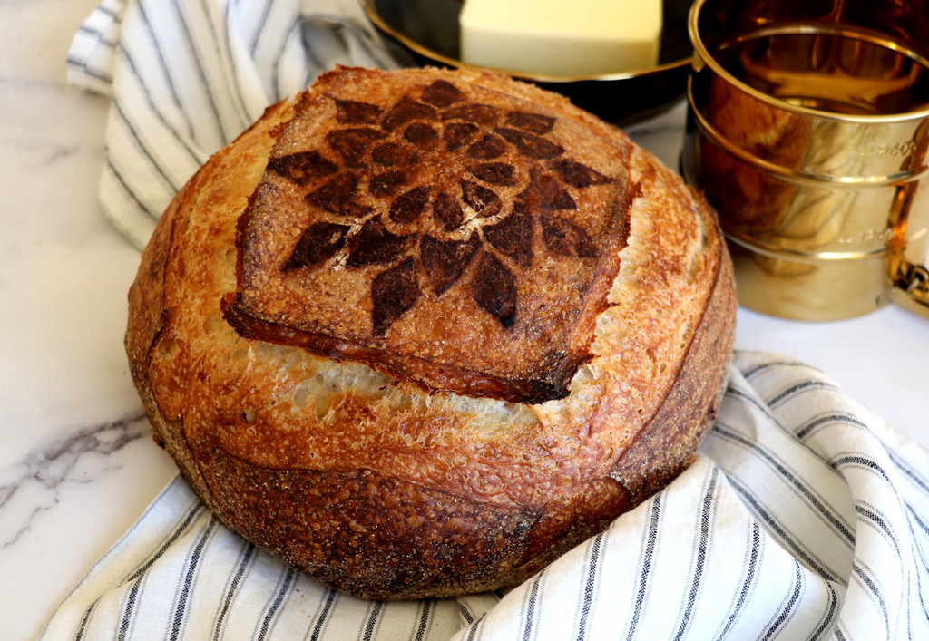 Cocoa powder bread stencil on sourdough boule with linen proofing cloth and flour sifter butter