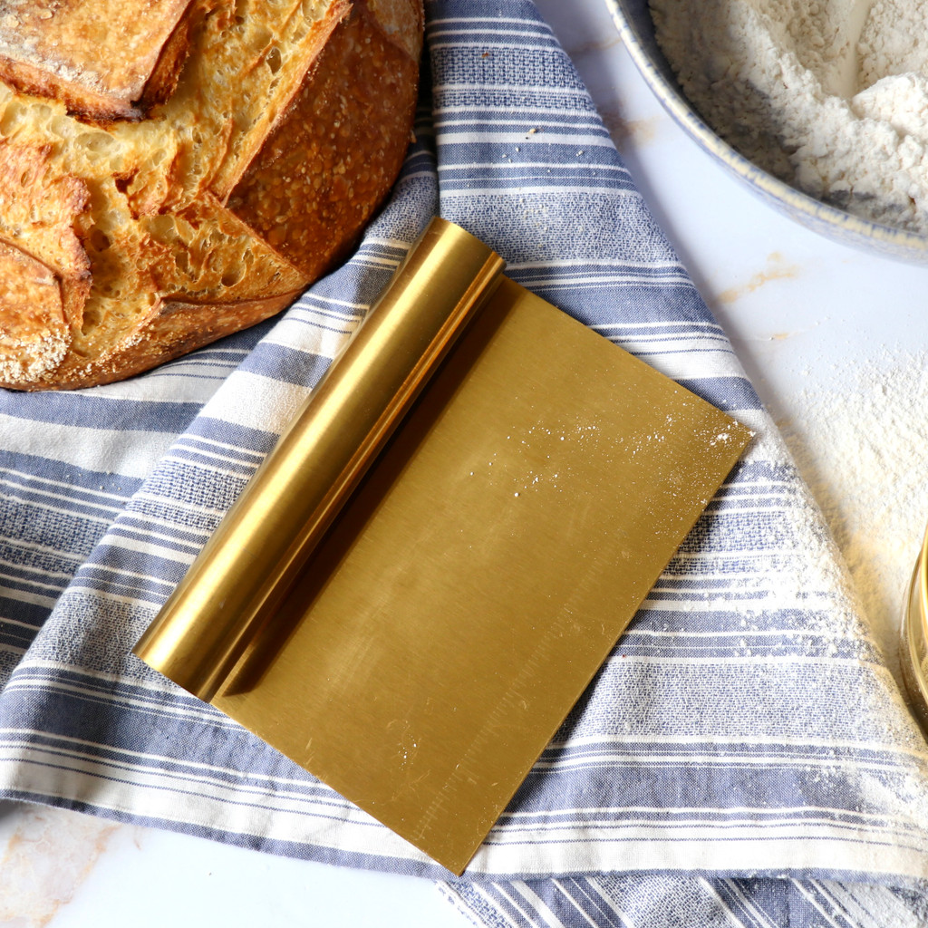 Golden bench scraper with ruler artisan bread boule flour and blue towel