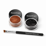 Angled view of Sweet Face Minerals Confusion black and Curious brown mineral eyeliners in clear jars with branded black lids, paired with a professional angled eyeliner brush. The finely milled powders showcase smooth, highly pigmented formulas designed for precise liner application.