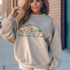 Model wearing beige occupational therapy sweatshirt with colorful flowers and “Helping you grow your own way” text.