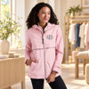 Woman wearing a pale pink New Englander rain jacket with a gray embroidered chest monogram and reflective trim in a boutique.