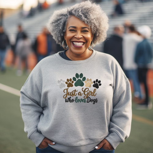 Woman wearing a gray “Just a Girl Who Loves Dogs” sweatshirt with paw print design, smiling outdoors at a sports field.