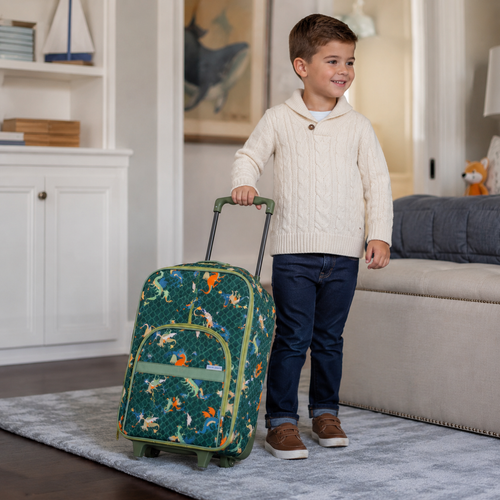 Little boy standing with a green dragon rolling suitcase with olive trim