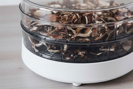 Side view of a food dehydrator with trays of sliced shiitake mushrooms drying at low temperature