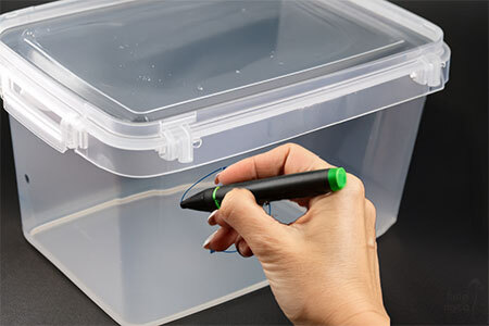 Hands using a marker pen to mark two 65mm circles on the side of a clear plastic storage tote, with masking tape applied around the marked area