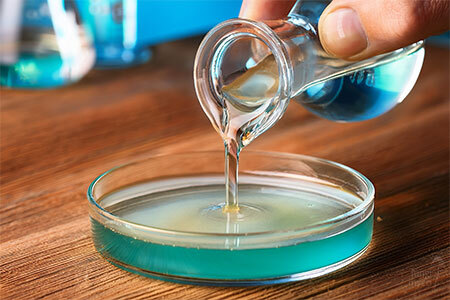 Person pouring warm liquid agar from a glass flask into a petri dish
