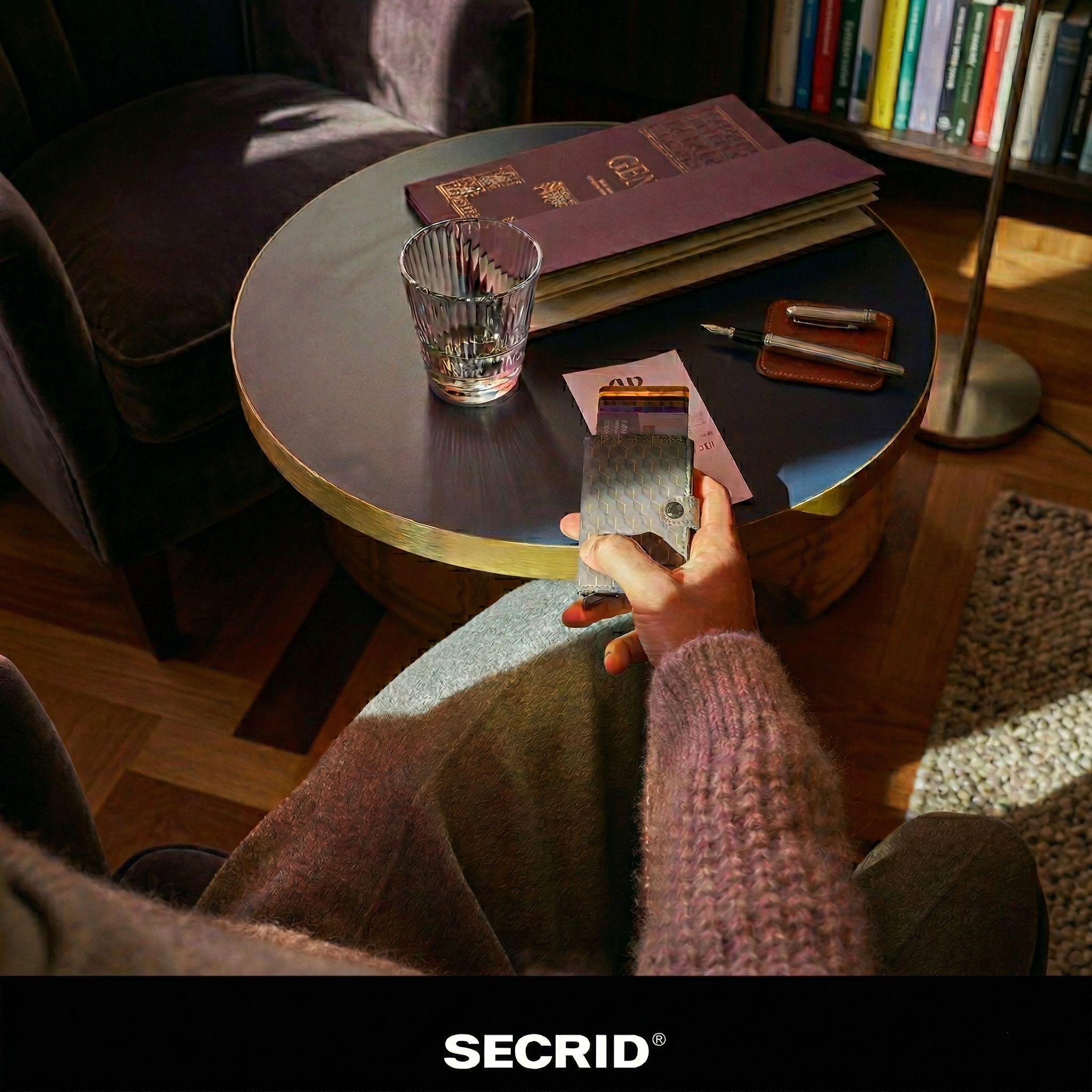 Secrid Miniwallet with a textured geometric pattern held in a lifestyle setting featuring a round table, crystal glass, and fountain pen.