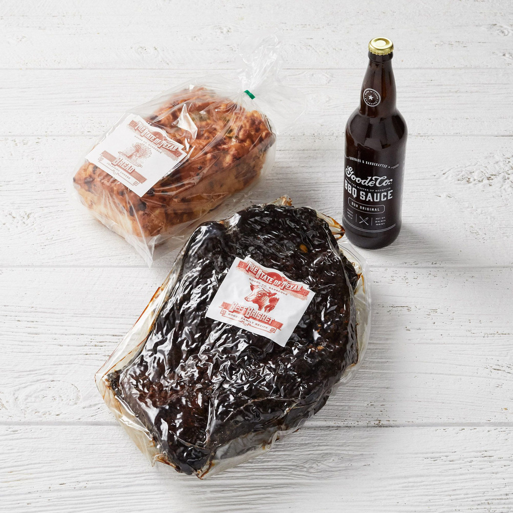 Vacuum-sealed packaging for Goode Co's Classic Mesquite Smoked Brisket with a glass bottle of BBQ sauce, and a loaf of jalapeño cheese bread.