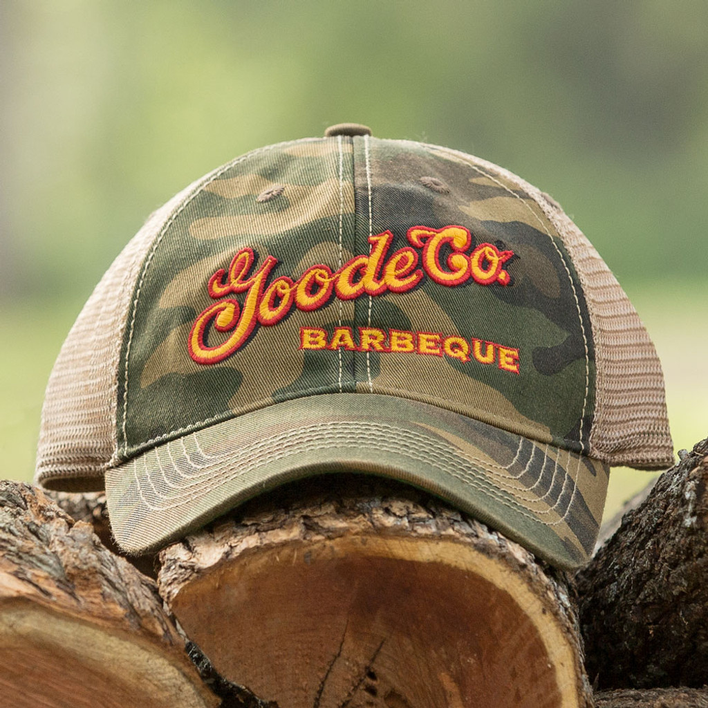 Goode Co's vintage camo trucker hat resting on Texas mesquite wood.
