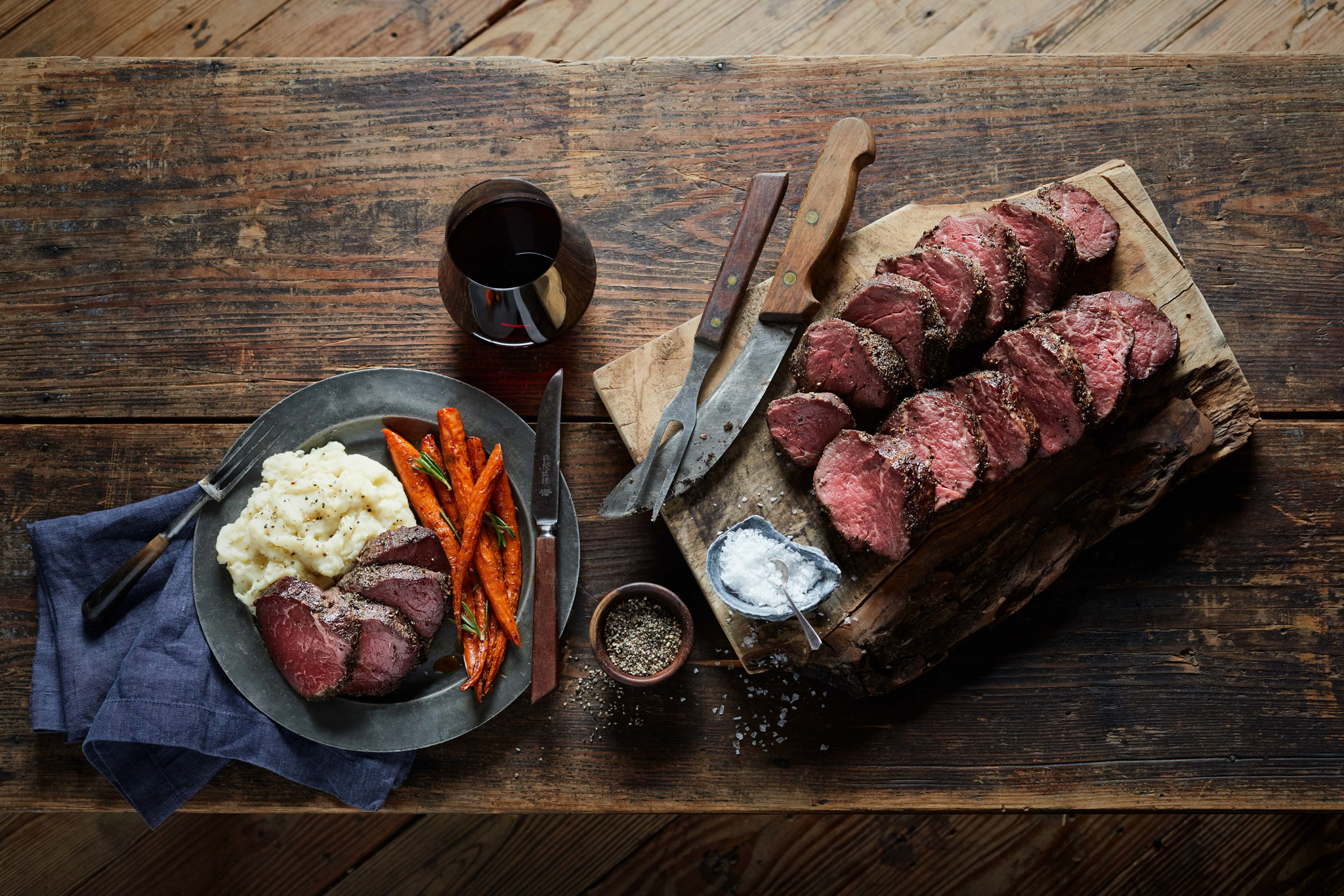 Sliced beef tenderloin, cooked medium rare, laid on a wooden cutting board next to a plate with a serving of beef and vegetables.