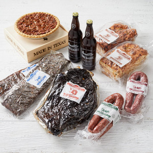 Shipping packaging of vacuum-sealed brisket, 2 slabs of ribs, 4 links of Texas sausage, 2 BBQ sauce bottles, and 2 loaves of jalapeño cheese bread, and our Brazos Bottom Pecan Pie in a wooden gift box.