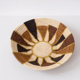 Large Helios Basket - A stunning collection of baskets on display or elevate your tablescape with a unique centerpiece. A simple yet bold basket from our Black & Natural collection. Handcrafted by women artisans living in Central Uganda who are part of a cooperative that provides employment and training for disadvantaged or marginalized communities - particularly widows, the disabled and those living with HIV/AIDS. * Made from all natural, sustainably sourced raffia and banana fibers * All synthetic AZO free dyes * Hanging loop on back allows basket to be wall decor in addition to tabletop use * Weavers hand make each basket from home while tending to other household duties | Details: Made in Uganda 18″ x 18″ x 5″ (45.7 x 45.7 x 12.7 cm)