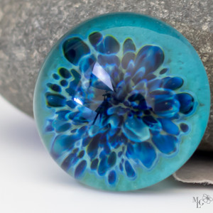 Happy medium blue petals imploded into the center of a boro glass cabochon. The background color is a cheery aqua. It's so pretty you'll want to sink into its depths. 23mm
