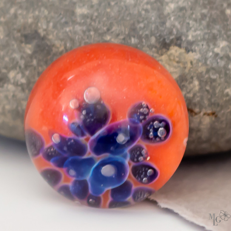 Lampwork glass cabochon in warm orange with cerulean blue bubbles nestled within a smooth, polished surface. The depths captivate the eye and draw you in for a closer look. 16mm