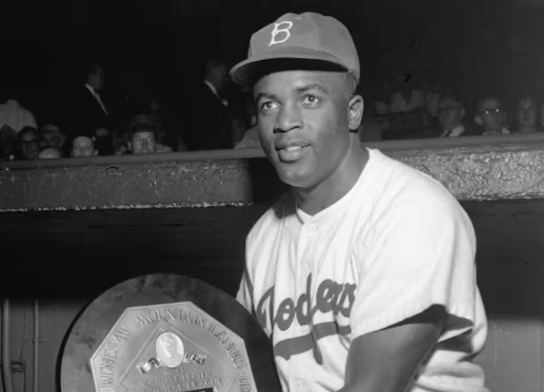 Black and white image of Jackie Robinson kneeling while holding a baseball award