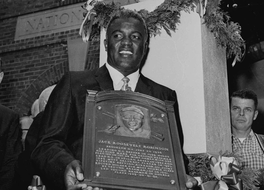 Black and white image of Jackie Robinson holding his MLB Hall of Fame plaque while in front of a baseball monument