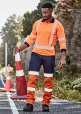 Hi-vis orange and navy work pants with reflective tape, worn by a man holding a traffic cone on a rural road.