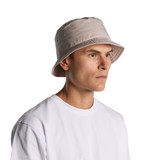A faded beige bucket hat with a soft brim, worn by a person in a white t-shirt. The hat features a logo.