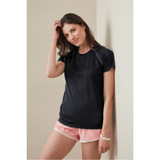 A woman in a black active t-shirt poses against a wall, wearing pink shorts. The shirt features short sleeves and has a logo.
