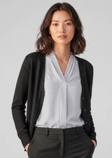 A black knit cardigan worn over a light blue blouse, styled with tailored black trousers. The model has shoulder-length hair.