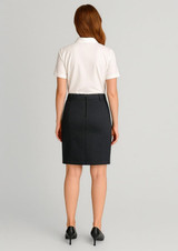 A woman in a white polo shirt and dark mid waist stretch chino skirt, facing away from the camera.