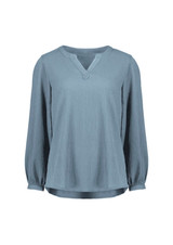 A light blue long sleeve blouse featuring a V-neck and ruché detailing. The blouse has a subtle texture and a relaxed fit.