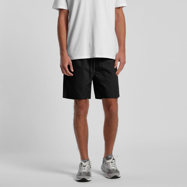 Black sports shorts with an elastic waistband, modelled by a person wearing a white t-shirt and grey sneakers.