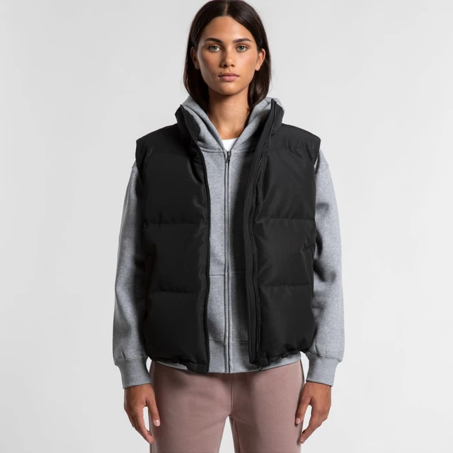 A black puffer vest worn over a grey hoodie, featuring a zip front and a logo. Model stands against a plain background.