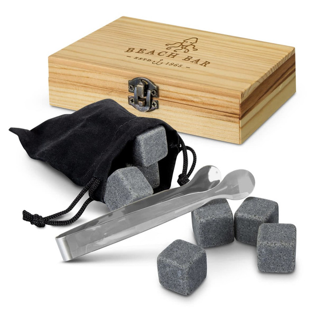 A wooden box containing grey whiskey stones, a black pouch, and silver tongs. The box features a logo.