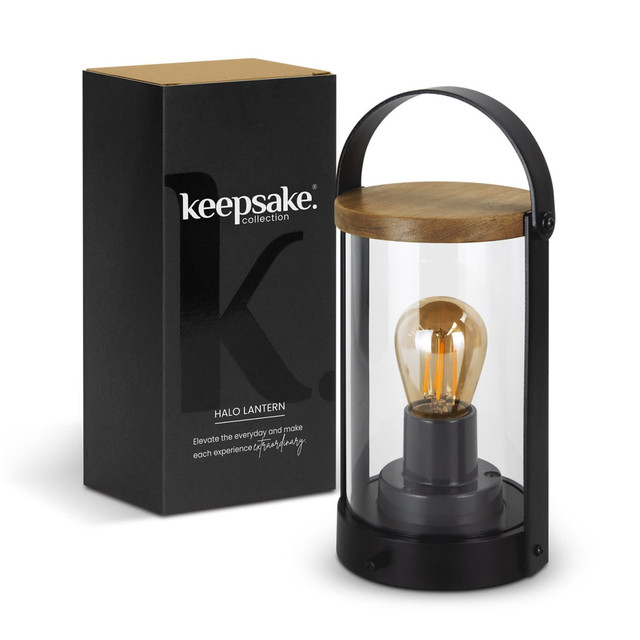 A black and clear glass lantern with a wooden lid, displayed alongside its packaging. Features a warm light bulb inside.