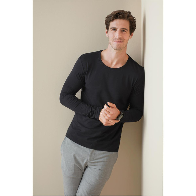 A black long sleeve shirt displayed on a man leaning against a wall, paired with light-coloured pants.