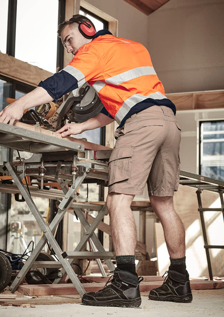 Curved cargo shorts in a light tan colour, worn by a man working on a construction site with ear protection.