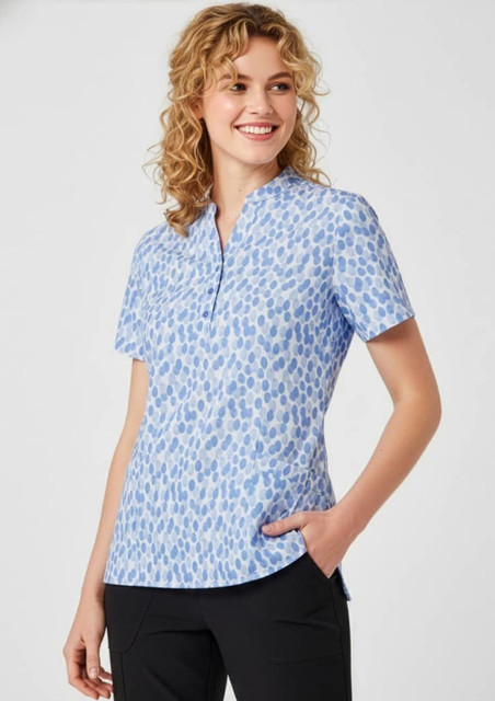 A blue tunic with a stardust print, featuring short sleeves and a collar, displayed on a smiling model.
